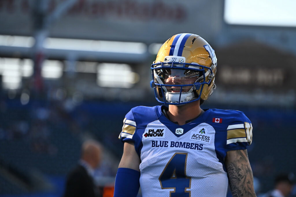 A football player wearing a Blue Bombers uniform and helmet stands on the field during a game.