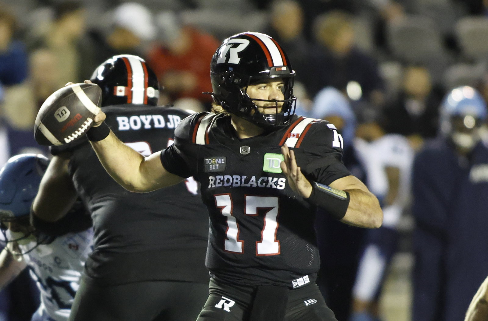 A football player in a black jersey with the number 17 and "REDBLACKS" on the front is preparing to throw the ball during a game.